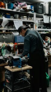 A man focused on work in a cluttered repair shop with various tools and equipment.